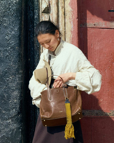 Small Yore Duffle Bag in Sandal brown leather with yellow tassel, carried by a woman.