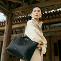 Black pebbled leather Small Yore Tote Bag with gold hardware and Songmont logo, worn by a woman.