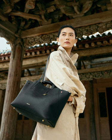Black pebbled leather Small Yore Tote Bag with gold hardware and Songmont logo, worn by a woman.