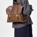 Large Shan Briefcase in Sandal, vegetable-tanned leather with gold hardware and buckle closure, worn as backpack.