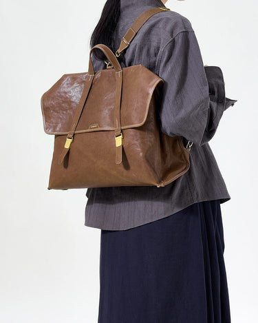 Large Shan Briefcase in Sandal, vegetable-tanned leather with gold hardware and buckle closure, worn as backpack.