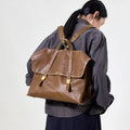 Large Shan Briefcase in Sandal brown vegetable-tanned leather with gold hardware, worn as a backpack by a woman.