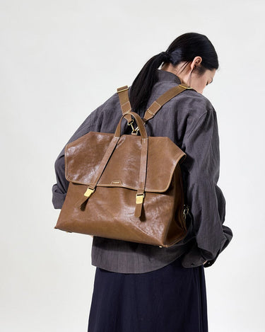 Large Shan Briefcase in Sandal brown vegetable-tanned leather with gold hardware, worn as a backpack by a woman.