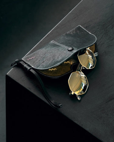 Yore Glasses Case: Black leather, white stitching, gold-rimmed sunglasses, reflective gold lenses, snap closure.
