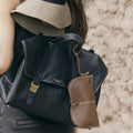 Black Yore glasses case with gold buckle, brown leather glasses case attached, on a woman wearing a sun visor.