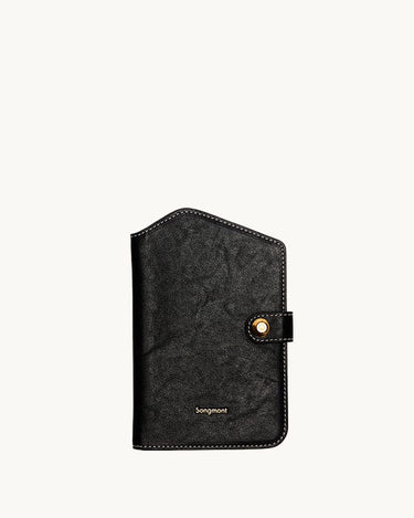 Black Songmont Yore Passport Case in vegetable-tanned leather with gold snap closure and white stitching.