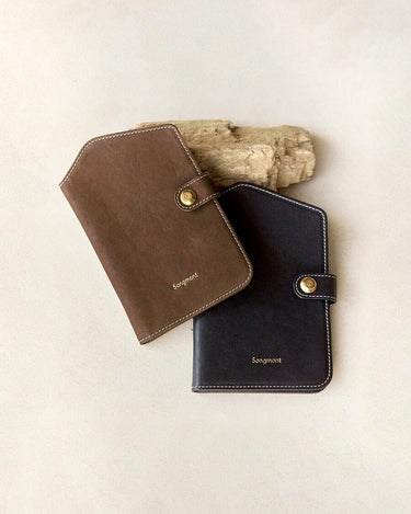 Yore Passport Case in brown and onyx, vegetable-tanned leather with gold snap closure and white stitching.