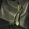 Olivine Tranquil Crystal Charm with braided leather, turquoise beads, and raw crystal on a dark green leather bag.