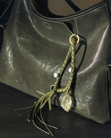Olivine Tranquil Crystal Charm with braided leather, turquoise beads, and raw crystal on a dark green leather bag.