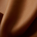 Close-up of caramel-colored full-grain leather with visible grain texture, showcasing the material of the Wish Seeds Charm.