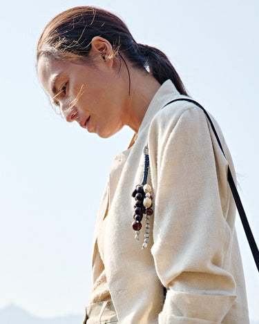 Wish Seeds Charm in denim color, featuring natural Bodhi seeds and a leather cord, attached to a woman's light jacket.
