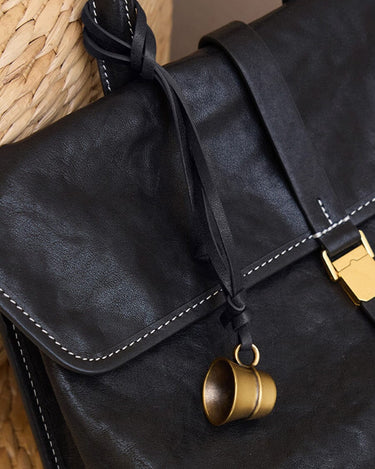 Worry-Free Cup Charm: Black leather bag with brass thimble charm, adjustable strap. Vegetable-tanned leather.