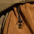 Worry-Free Cup Charm: brass rings on black leather cord against tan suede material. Alloy hardware.