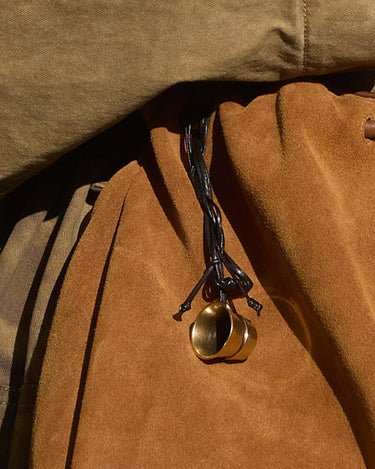 Worry-Free Cup Charm: brass rings on black leather cord against tan suede material. Alloy hardware.