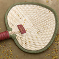 Woven fan charm made of palm fronds with dark green trim and leather handle. Features 'Songmont' tag.