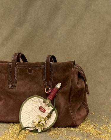 Woven fan charm with floral detail on brown suede tote bag. Songmont accessory.