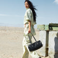 Woman in light green outfit carries black Yore Baguette Bag in desert setting