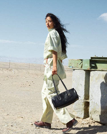Woman in light green outfit carries black Yore Baguette Bag in desert setting