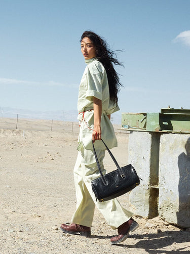 Woman in light green outfit carries black Yore Baguette Bag in desert setting