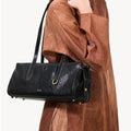 Black Yore Baguette Bag in Onyx with gold hardware and white stitching, worn by a woman in a brown dress.