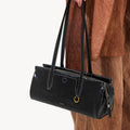 Black Yore Baguette Bag by Songmont, crafted from vegetable-tanned leather with white stitching and gold hardware.