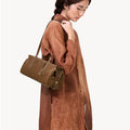 Yore Baguette Bag in Sandal color, a structured olive-brown leather shoulder bag carried by a woman in a brown dress.