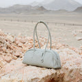 Light grey full-grain leather Yore Toast Bag with SS 304 vacuum electroplated hardware on rocks.