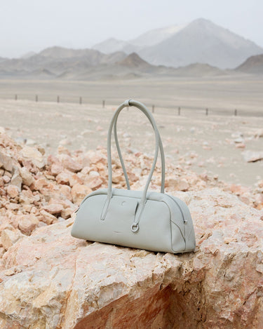 Light grey full-grain leather Yore Toast Bag with SS 304 vacuum electroplated hardware on rocks.
