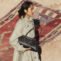 Yore Toast Bag in Ebony Nappa leather with white stitching, held by a woman in a trench coat.