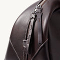 Close-up of Songmont Yore Toast Bag in Ebony, featuring dark Nappa leather, white stitching, and embossed logo zipper pull.