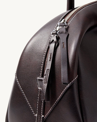 Close-up of Songmont Yore Toast Bag in Ebony, featuring dark Nappa leather, white stitching, and embossed logo zipper pull.