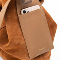 Songmont medium drippy tote bag in caramel with suede exterior and leather pocket holding a smartphone.