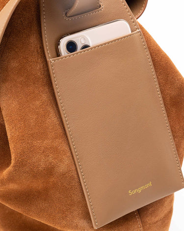 Songmont medium drippy tote bag in caramel with suede exterior and leather pocket holding a smartphone.